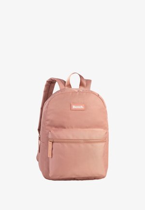 Sac à dos en tissu rose de forme arrondie, avec une poche zippée à l'avant et deux bretelles. Présente une étiquette de marque à l'avant.