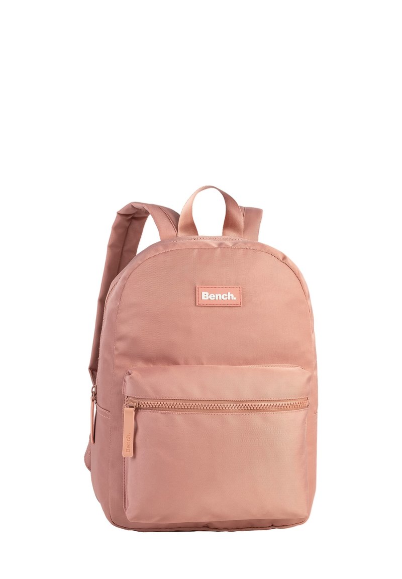 Sac à dos en tissu rose de forme arrondie, avec une poche zippée à l'avant et deux bretelles. Présente une étiquette de marque à l'avant.