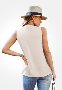 Beige mouwloos topje met een gestructureerde afwerking, gecombineerd met blauwe jeans. Een strohoed met een donkere band wordt gedragen om de casual look te versterken.
