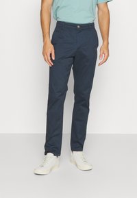 Marineblå chinos lavet af bomuld, med lige ben-design, forlommer og knaplukning, parret med lyse sneakers.