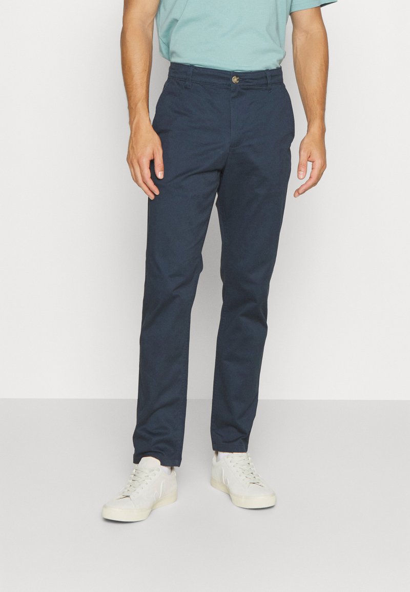 Marineblå chinos lavet af bomuld, med lige ben-design, forlommer og knaplukning, parret med lyse sneakers.