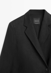 Zwart op maat gemaakt colbert met inkeping op de revers en een enkelvoudige knoopsluiting, met een "Massimo Dutti" label aan de binnenkant van de kraag.