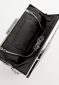 Kleine rechthoekige zilverkleurige clutch met een zwart stoffen interieur en een opgespoelde zilveren kettinkjesriem binnenin.