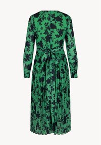 Groene bloemenjurk met lange mouwen, strikdetail op de rug, vloeiende plooien en zwart bloemenpatroon op lichte stof.