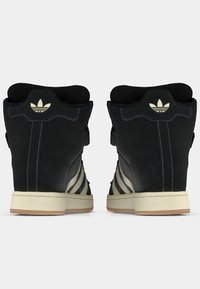 Ψηλά αθλητικά παπούτσια κατασκευασμένα από μαύρο σουέντ με λεία υφή, με αντίθετες λευκές ρίγες και μπεζ λαστιχένιες σόλες. Διαθέτουν κεντημένο λογότυπο.