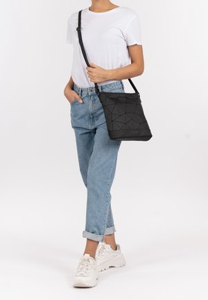 Černá crossbody taška s geometrickým vzorem, strukturovaným povrchem, nastavitelným popruhem a pevnou formou, vystavená na neutrálním pozadí.