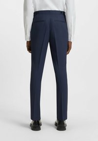 Pantaloni da abito blu navy con vestibilità slim, texture morbida, due tasche posteriori e vita con doppio bottone, abbinati a una camicia bianca a maniche lunghe.