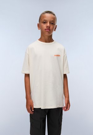 Beige cotton t-shirt with crew neck, short sleeves, and small orange logo on the left chest; paired with black cargo pants.