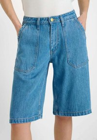 Lichtblauwe denim short met een hoge taille, twee frontzakken en contrasterende gele stiksels. Glad textuur, knielange snit en een messing knoop.