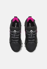 Chaussures de sport noires avec des accents roses, tige en mesh texturé, lacets réfléchissants et semelle en caoutchouc avec des picots de traction saillants.