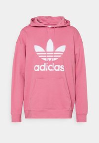 Rosa huvtröja i mjukt material, med en stor vit Adidas-logotyp och tre ränder på framsidan, samt en framficka och justerbar huva.