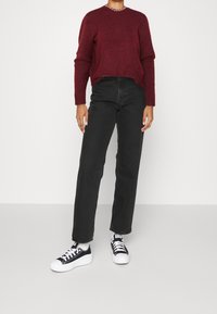 Maglione a maglia bordeaux, jeans neri a vita alta e gamba dritta, e sneakers in tela nera con suole bianche. Outfit semplice e informale.