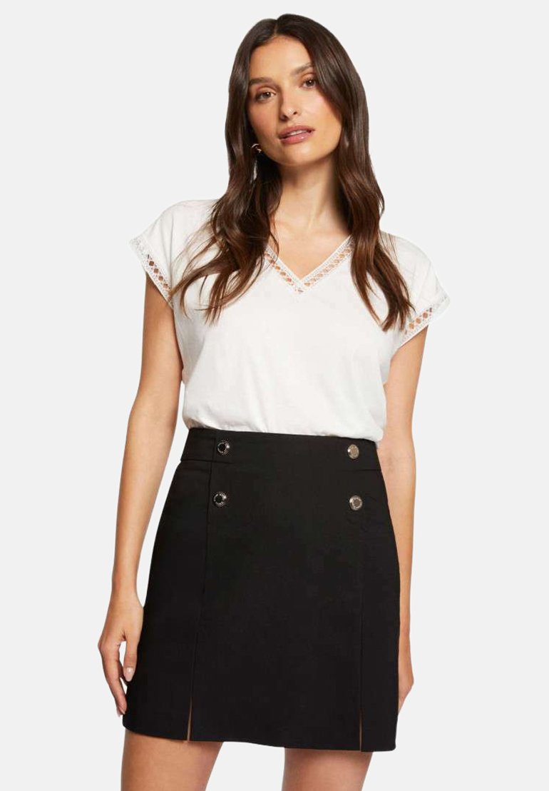 Haut blanc à col en V avec des bordures en dentelle, associé à une jupe noire taille haute avec des accents de boutons en métal argenté et des fentes sur les côtés.