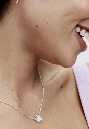 Collana in argento con pendente a forma irregolare in pietra bianca, abbinata a una tonalità di pelle sobria e a un top morbido viola.