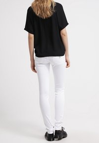 Black short-sleeved blouse with a loose fit paired with white skinny jeans and black lace-up shoes, viewed from the back.