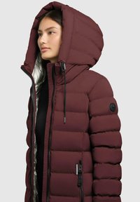 Bordeauxfarbene Pufferjacke mit großer Kapuze, Reißverschluss vorne und strukturiertem Steppdesign. Verfügt über schwarze Beschläge und ein reflektierendes Innenfutter.