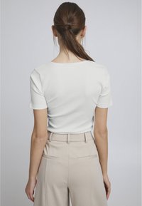 Hvid ribbet tætsiddende top med korte ærmer, parret med højtaljede beige bukser med baglommer og en glat tekstur.