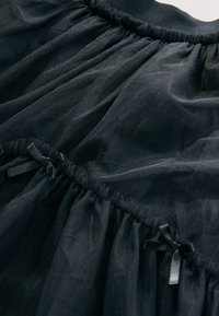 Gonna in tulle nero con vita arricciata e piccoli fiocchi di raso. Tessuto morbido e trasparente con una texture fluida, caratterizzato da più balze.