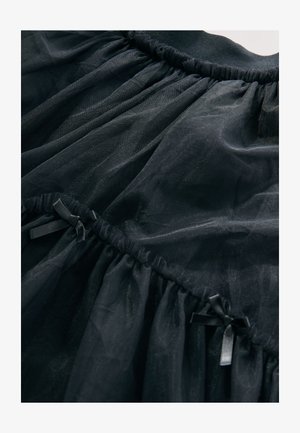 Črno krilo iz tila z nabranim pasom in majhnimi satenastimi pentljami. Mehka, prosojna tkanina s tekočo teksturo in več plastmi volanov.