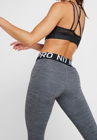 Soutien-gorge de sport noir avec des détails en maille et des fines bretelles, associé à un legging gris avec un motif texturé et une taille élastique noire.