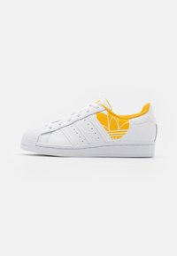Vita lädersneakers med gula accenter, som har tre sidosträck, en strukturerad tåsula och en upphöjd logotyp på den yttre sidan.