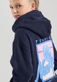 Tummansininen huppari, jossa on suuri vaaleanharmaa tennisaiheinen grafiikka selässä. Pehmeä tekstuuri, ribbaatut hihansuut ja helma. Säädettävä huppu.