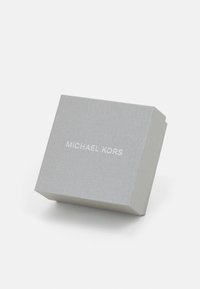 Cutie pătrată texturată argintie cu capac, având numele brandului "MICHAEL KORS" în alb, centrat pe față.