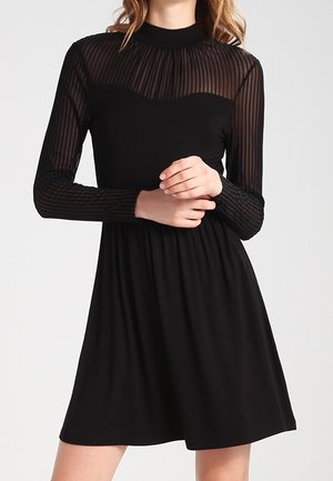 Schwarzes Kleid mit langen, durchsichtigen, plissierten Ärmeln und tailliertem Oberteil, das sich in einen lockeren Rock ausweitet und einen hohen Kragen hat.