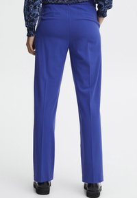 Blauwe op maat gemaakte broek met een rechte pijpdesign, achterzakken en een gladde textuur. Inclusief zwarte schoenen aan de onderkant.