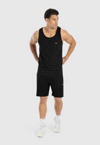 Conjunto de top sin mangas negro y pantalones cortos, hecho de tejido suave. Presenta una marca mínima en el pecho y el muslo. Combinado con zapatillas deportivas blancas y calcetines.