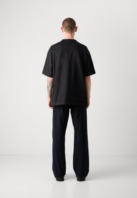 T-shirt en coton noir à coupe décontractée, à manches courtes, avec un col rond et un design uni, associé à un pantalon ample bleu foncé.