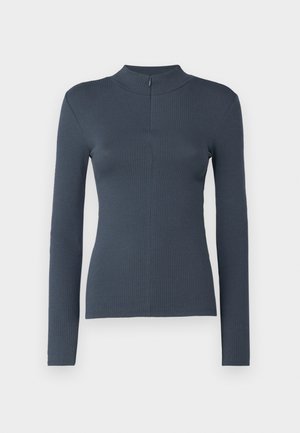 Dugi rukav u tamnosivom rebrastom materijalu, sa visokom ovratnikom i zatvaračem na leđima. Prilagođen oblik s suptilnim detaljima šavova.