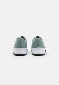 Zapatillas deportivas en gris-verde con un upper de tela texturizada, suela blanca y detalles en negro en el talón y en la lengüeta.