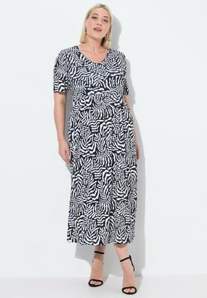 Maxi jurk in zwart-wit zebra print, korte mouwen, v-hals, zachte stof, vloeiende silhoeet, enkellang, gecombineerd met zwarte hakken.