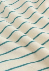 Pehmeä kangas, jossa valkoinen tausta ja teal-väriset aaltoilevat viivat. Näyttää sileältä tekstuurilta, jossa on neulekuvio ja lempeät taitokset, jotka luovat syvyyttä.