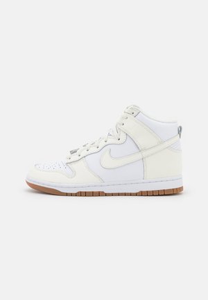 White high-top sneakers with leather material, padded collar, perforated toe box, and gum rubber sole. Features stitched accents and logo.