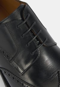 Zwarte leren nette schoen met een ronde neus, voorzien van decoratieve brogue perforaties en zes gaten voor veters. Gladde textuur en gepolijste afwerking.