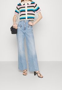 Virkat randigt linne i blått, grönt, svart och rosa med krage; matchat med ljusblå vida jeans och svarta sandaler med remmar.