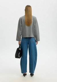 Hall hallike kraeitud dressipluus, laiad sinised teksad, must käekott unikaalse sangaga, teravaotstega mustad kontsakingad, nähtavad sirged pikad juuksed.