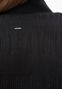 Tissu noir texturé avec des plis verticaux et une petite épingle barre argentée horizontale près du centre supérieur.