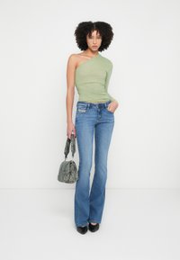 Heleroheline üheõlaline top kogutud tekstuuriga, sobitatud figuurile rõhutatud siniste lehvivate teksadega, käes väike mustriline käekott, mustad teravad kontsakingad.