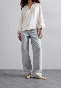 Blusa collared di un beige chiaro con maniche a sbuffo; abbinata a jeans larghi di un blu chiaro; scarpe beige a punta completano il look.