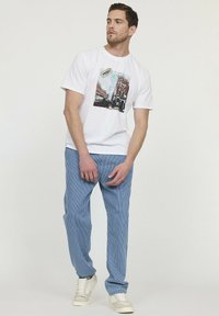 T-shirt en coton blanc avec un imprimé graphique d'un bâtiment; associé à un pantalon rayé bleu et blanc; portant des baskets blanches.