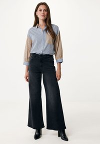 Camicia button-up a righe blu chiaro e beige con maniche arrotolate, abbinata a jeans neri a vita alta e gamba larga e stivali neri con tacco.