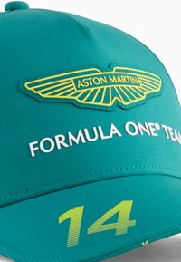 Gorra color agua con un logo amarillo de Aston Martin y el texto "FORMULA ONE® TEAM". Presenta el número "14" en verde brillante en la visera.