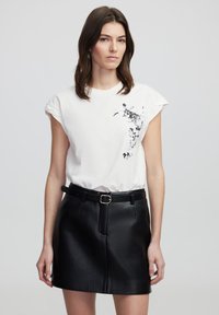 Witte katoenen t-shirt met korte omgerolde mouwen en zwarte bloemenprint aan de voorkant, gecombineerd met een hoge zwarte leren minirok.