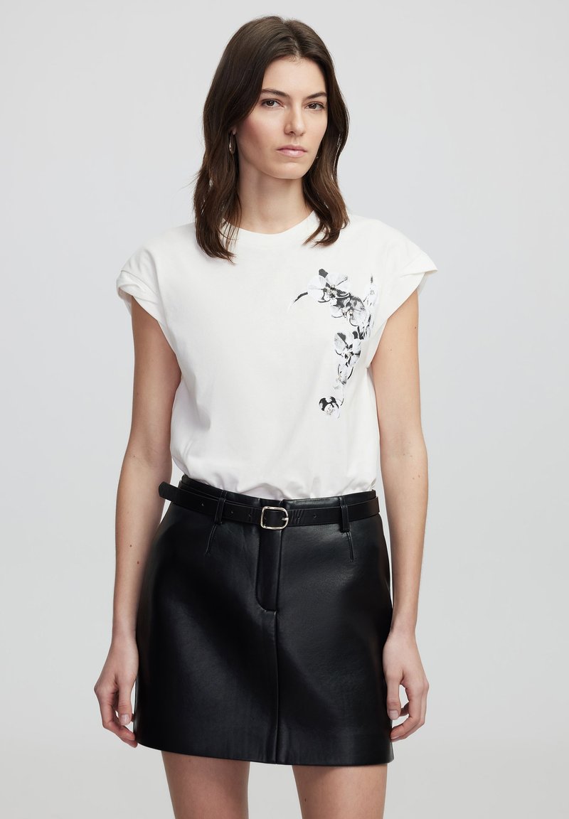 T-shirt en coton blanc à manches courtes roulées et imprimé floral noir sur le devant, associé à une mini-jupe en cuir noire taille haute.