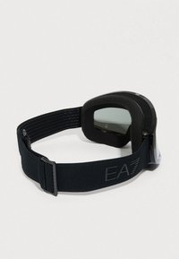 Μαύρα γυαλιά σκι με σκουρόχρωμους φακούς και ρυθμιζόμενο λουράκι με το λογότυπο EA7, απεικονίζονται σε απλό ανοιχτό φόντο.