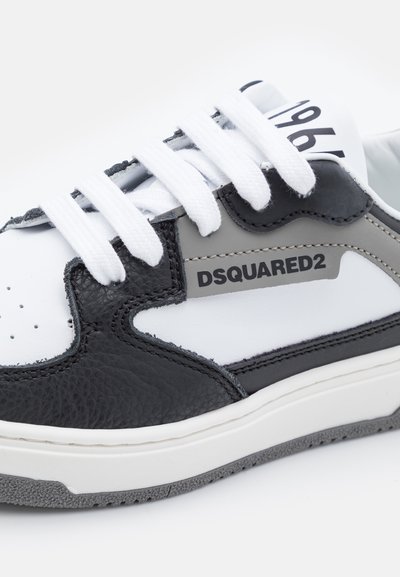 Sneaker bianco e nero realizzati in pelle e gomma, con una punta nera testurizzata, lacci bianchi e un pannello laterale grigio con logo.