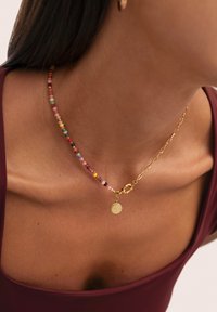 Collar de cuentas colorido hecho de cuentas pequeñas y redondas en rosa, verde, amarillo y azul, con una cadena dorada y un charm circular.